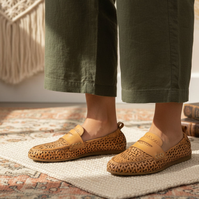 a woman wearing yellow tan loafer with perforated leather uppers standing on a rug in room.
